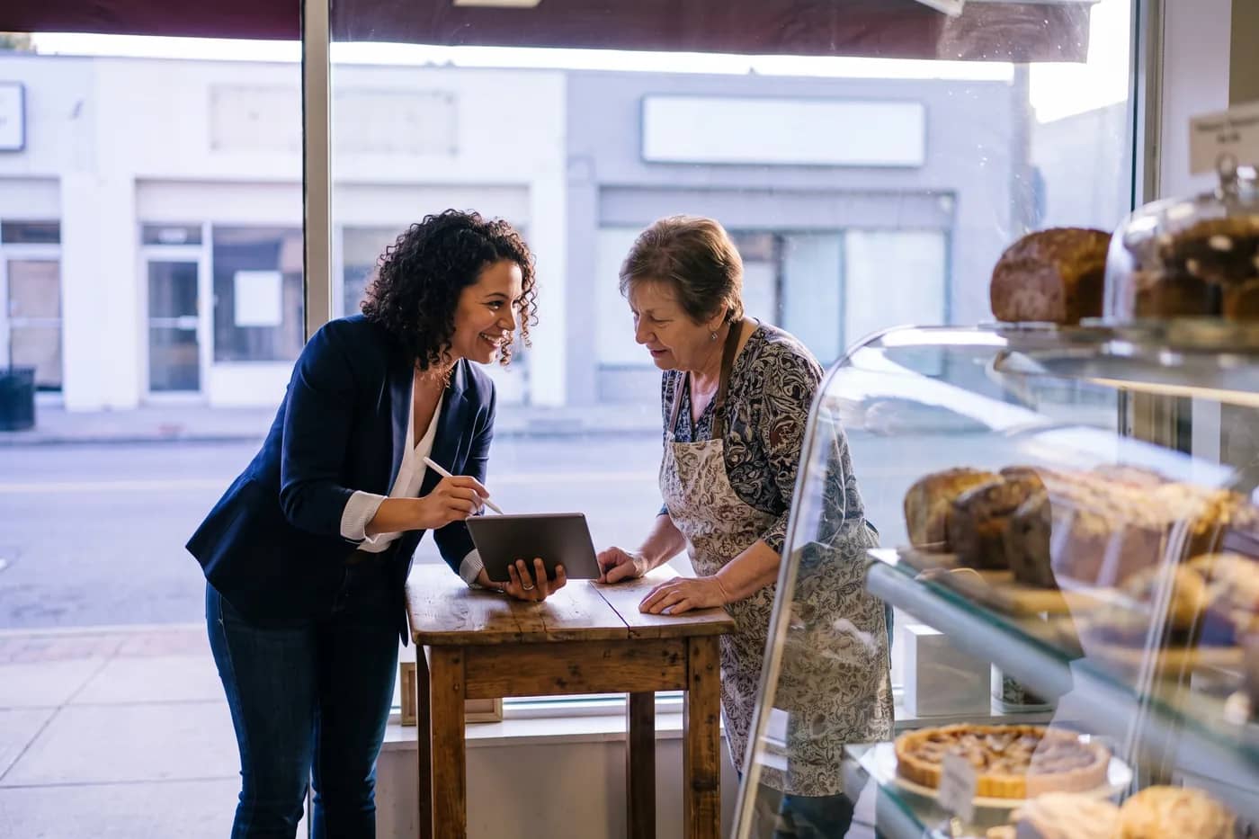 Consultora mostrando um plano no tablet à dona de uma padaria